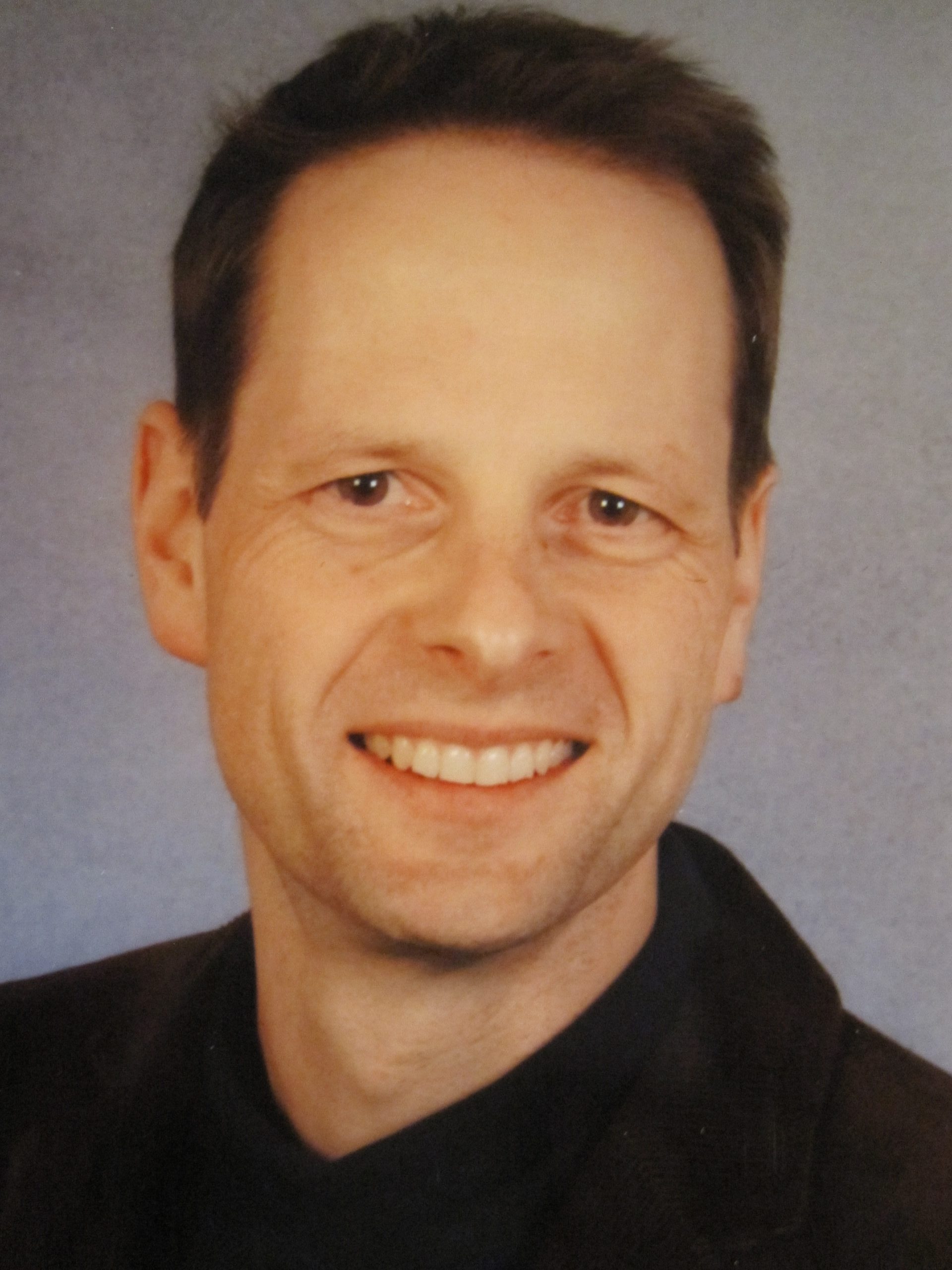 Close-up of a smiling man with short dark hair against a gray backdrop.